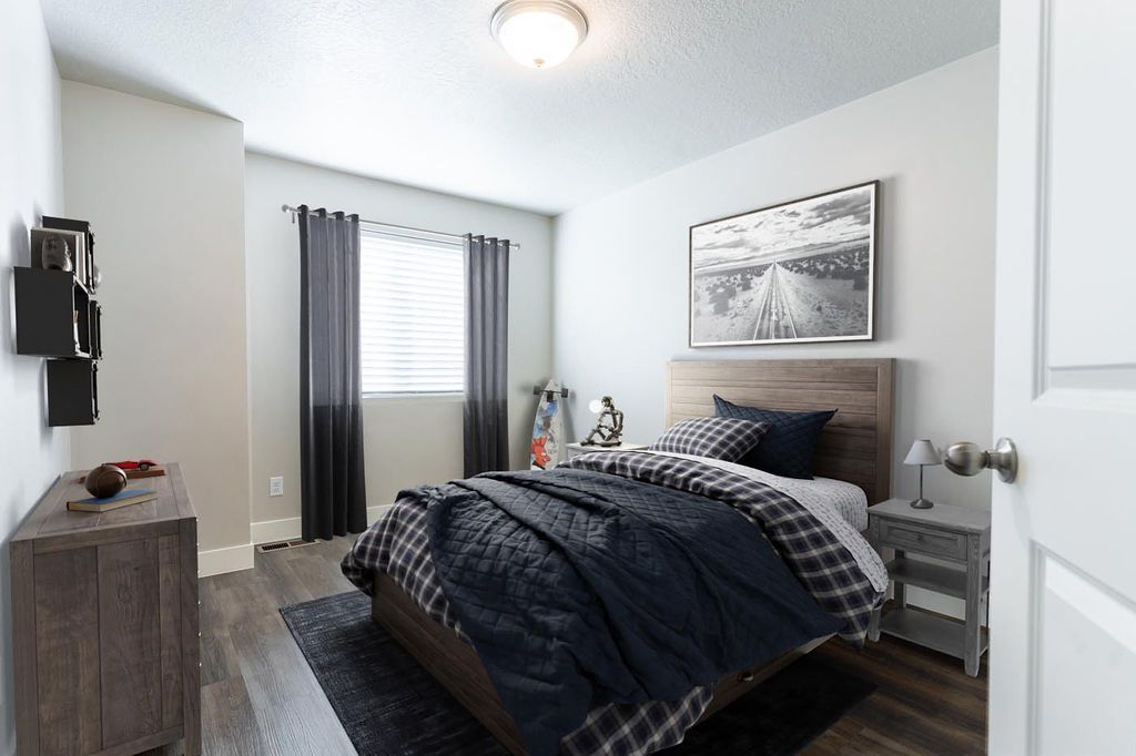 Bright bedroom with a made bed, dark bedding, gray curtains, and a framed wall print