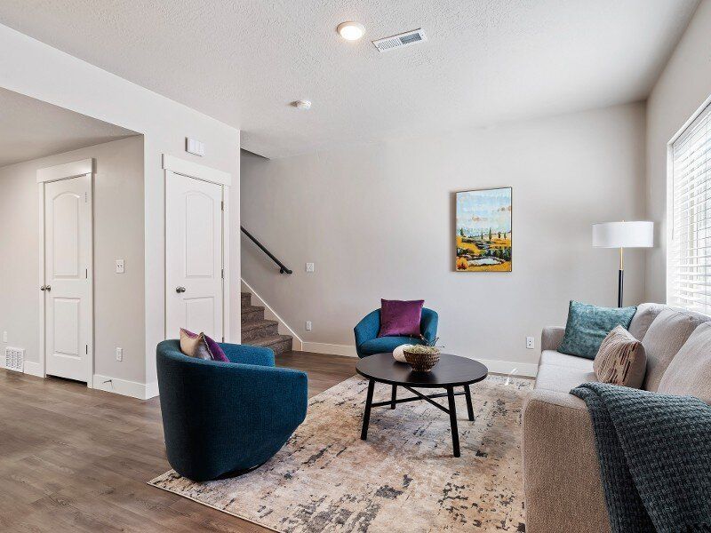 Living room with blue chairs, sofa, coffee table, rug, artwork, and staircase.