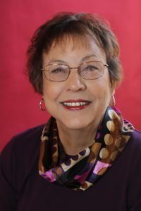 Portrait of a smiling woman with glasses and a patterned scarf against a red background