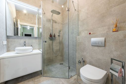 Modern bathroom with glass shower, wall-mounted sink, and toilet on beige tile walls and floor