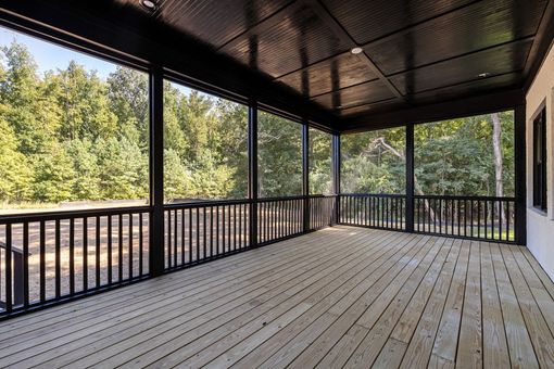 Covered wooden deck with black railings and a forest view beyond the open sides