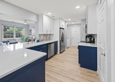 Bright modern kitchen with white cabinets, blue lower cabinets, stainless appliances, and light wood floors