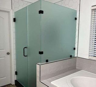 Glass shower enclosure beside a white bathtub in a modern tiled bathroom