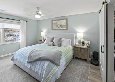 Bright bedroom with a bed, nightstands, lamps, window, and gray-blue decor
