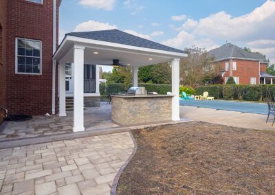 Covered outdoor courtyard with stone pavilion, brick building, paved walkway, and landscaped grounds