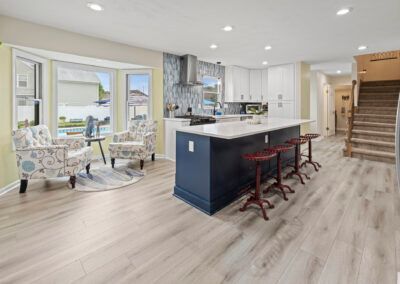 Bright modern kitchen with navy island, bar stools, dining nook, and staircase in an open-plan home