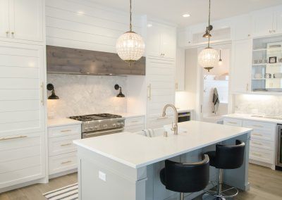 Bright white modern kitchen with island, pendant lights, stainless stove, and dark bar stools.