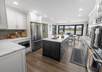 Bright modern kitchen with white cabinets, stainless appliances, dark island, and dining area by large windows