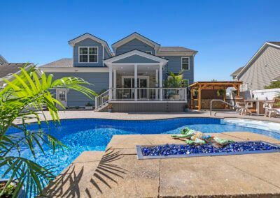 Backyard pool and patio with a two-story house, blue water, and a covered outdoor seating area