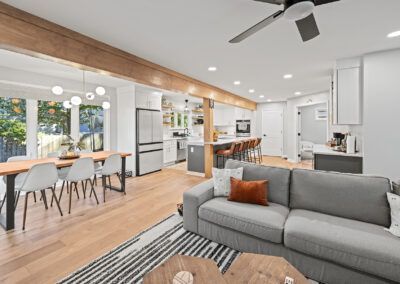Bright open-plan living room with gray sofa, wood accents, dining area, and modern kitchen