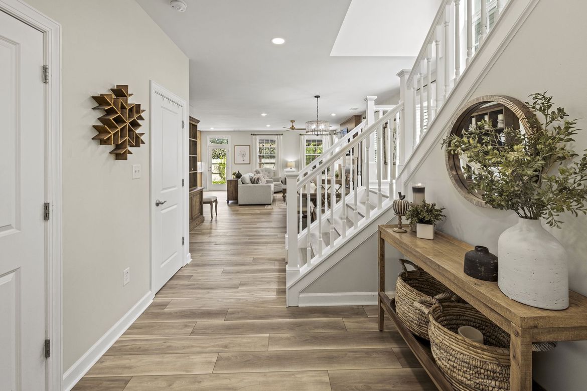 Bright hallway with wood flooring, white staircase, and console table with wreath décor leading to a living area