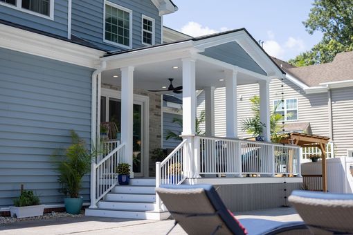 Back patio with white railings, steps, and a covered porch on a blue house