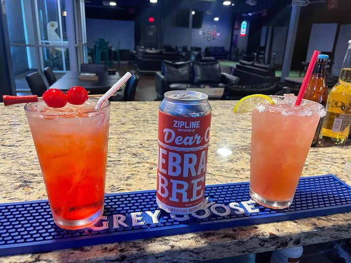 Three drinks are sitting on a bar next to a can of grey goose.