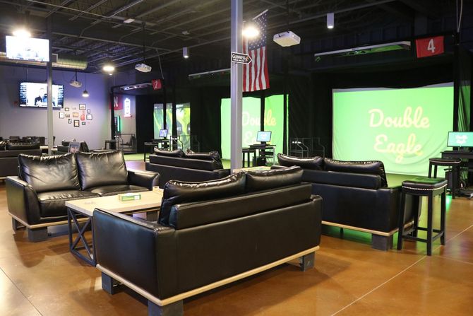 A room with a couch , chairs , a television and a golf simulator.