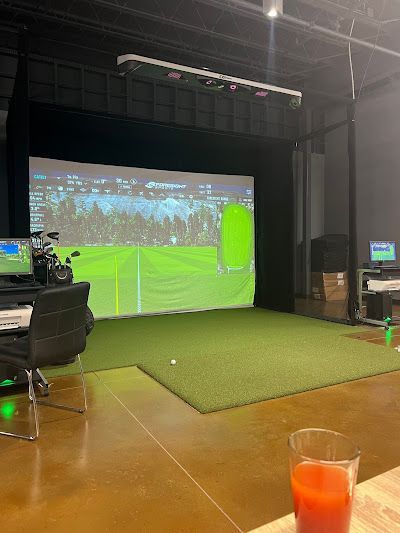 A golf simulator with a large screen and a glass of orange juice on a table.