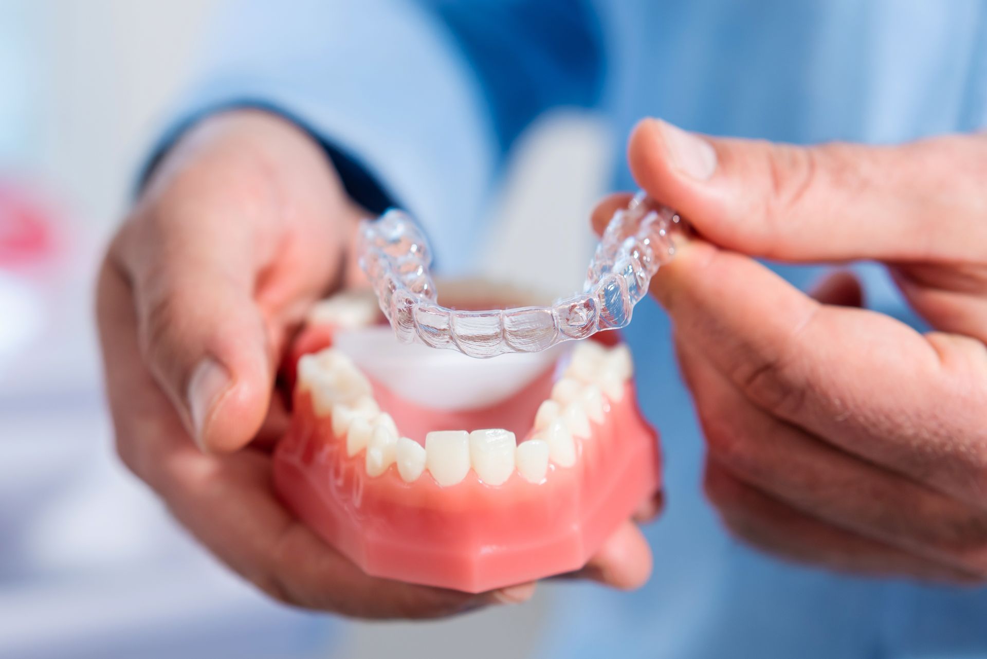 Hands holding a clear dental aligner above a set of model teeth.
