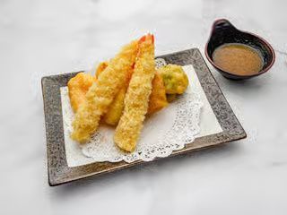 Tempura shrimp and vegetables on a white paper-lined plate with dipping sauce