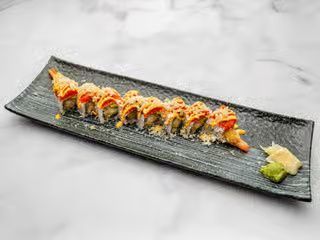Sushi roll topped with sauce and garnish on a black rectangular plate