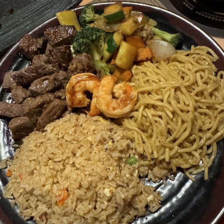 Platter with steak, shrimp, noodles, fried rice, and mixed vegetables on a dark plate
