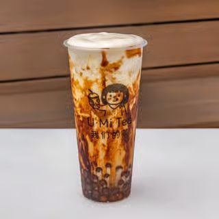Tall iced brown sugar milk tea in a clear cup with tapioca pearls and a logo on a white surface.