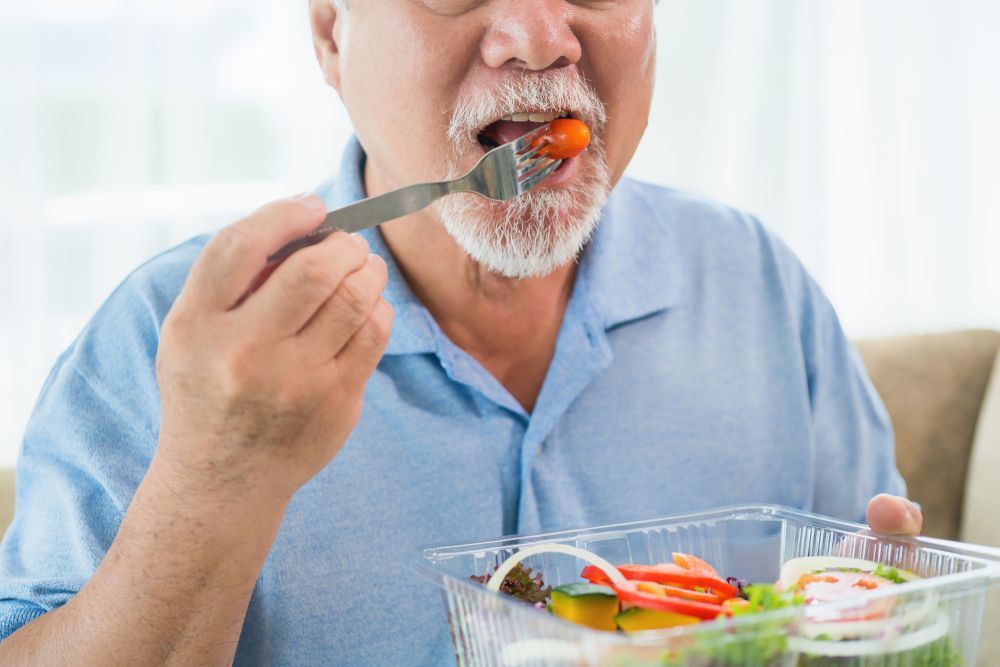 An Elderly Man is Eating a Salad With a Fork — Collis Care In Dundowran, QLD