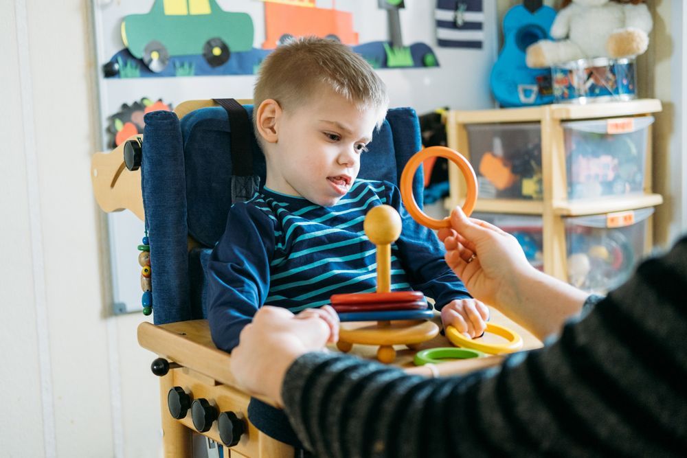 A Young Boy is Sitting in a High Chair Playing With a Toy — Collis Care In Dundowran, QLD