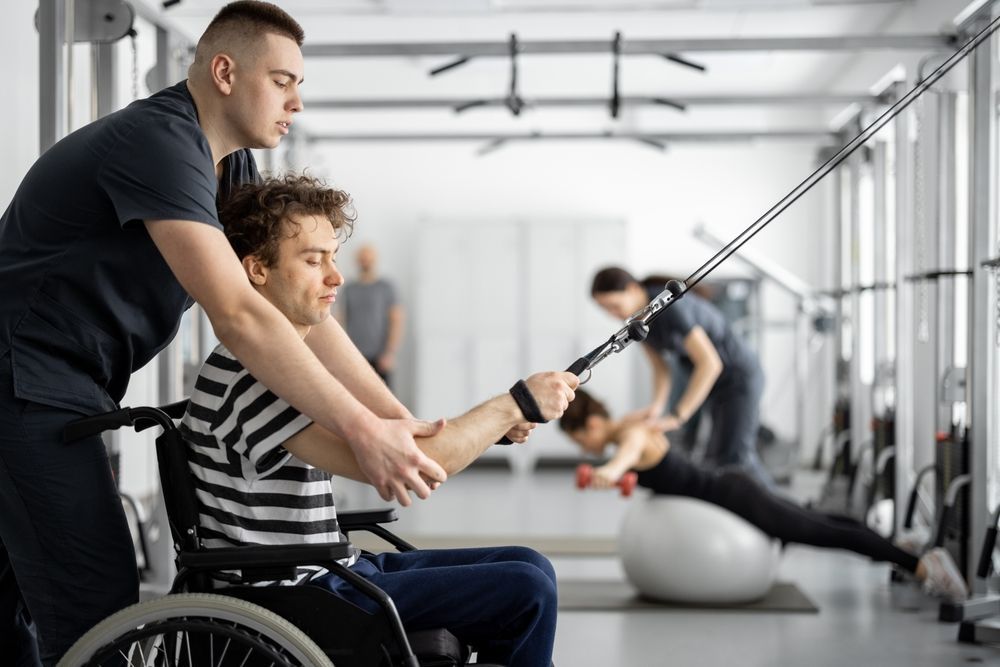A Man in a Wheelchair is Being Helped by a Man in a Gym — Collis Care In Dundowran, QLD