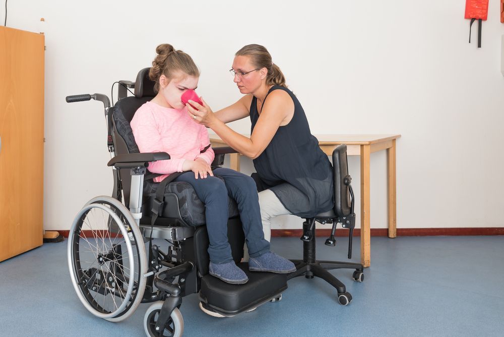 A Woman is Helping a Young Girl in a Wheelchair Drink From a Cup — Collis Care In Dundowran, QLD
