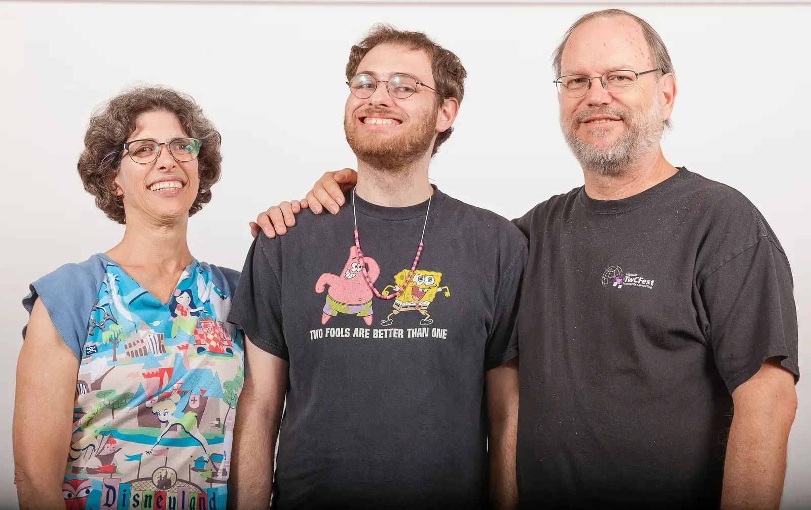Three people smiling, posed together: a woman, a man with his arm around another man wearing a SpongeBob shirt.