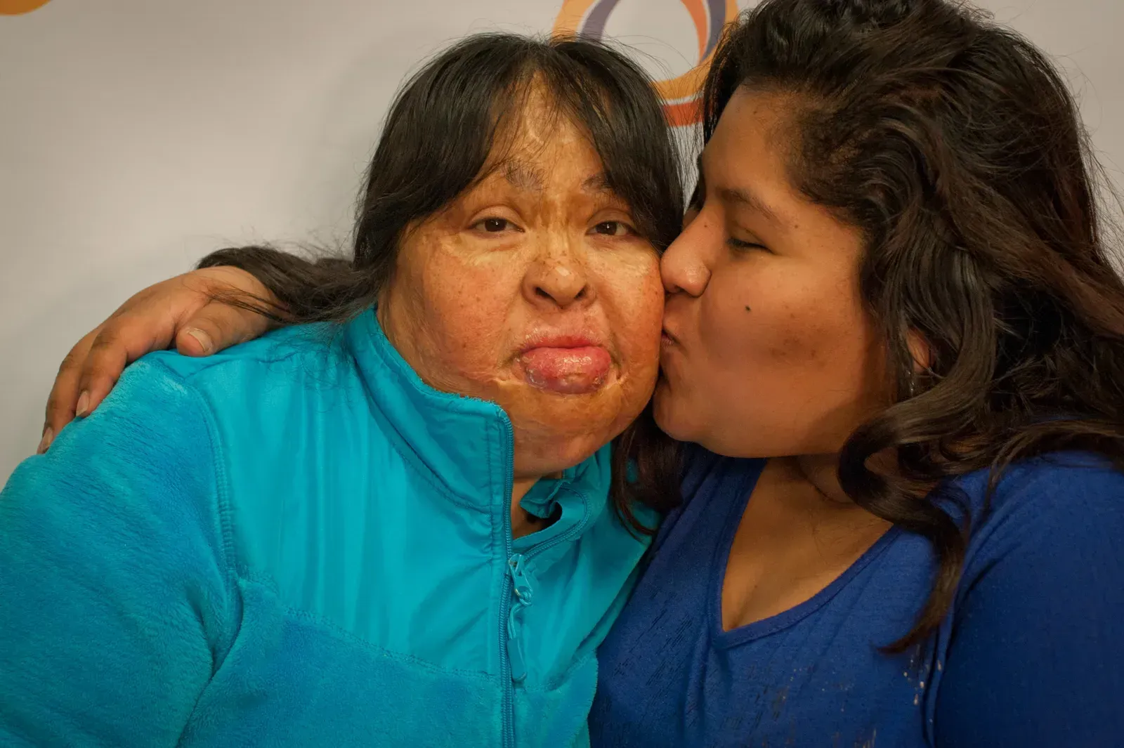 Woman in blue being kissed on the cheek by another woman, both smiling.