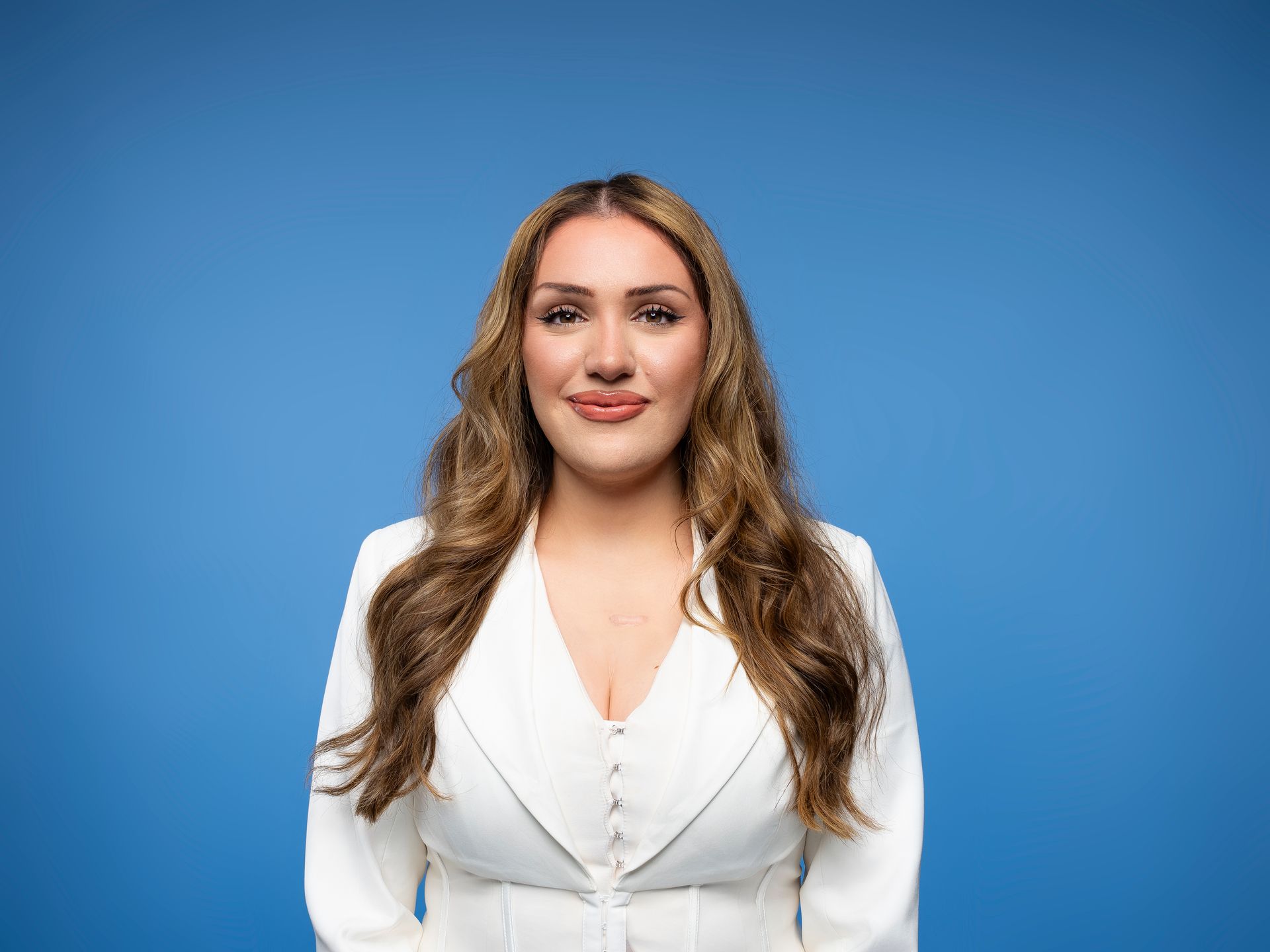Woman with brown hair smiling in a white blazer 
