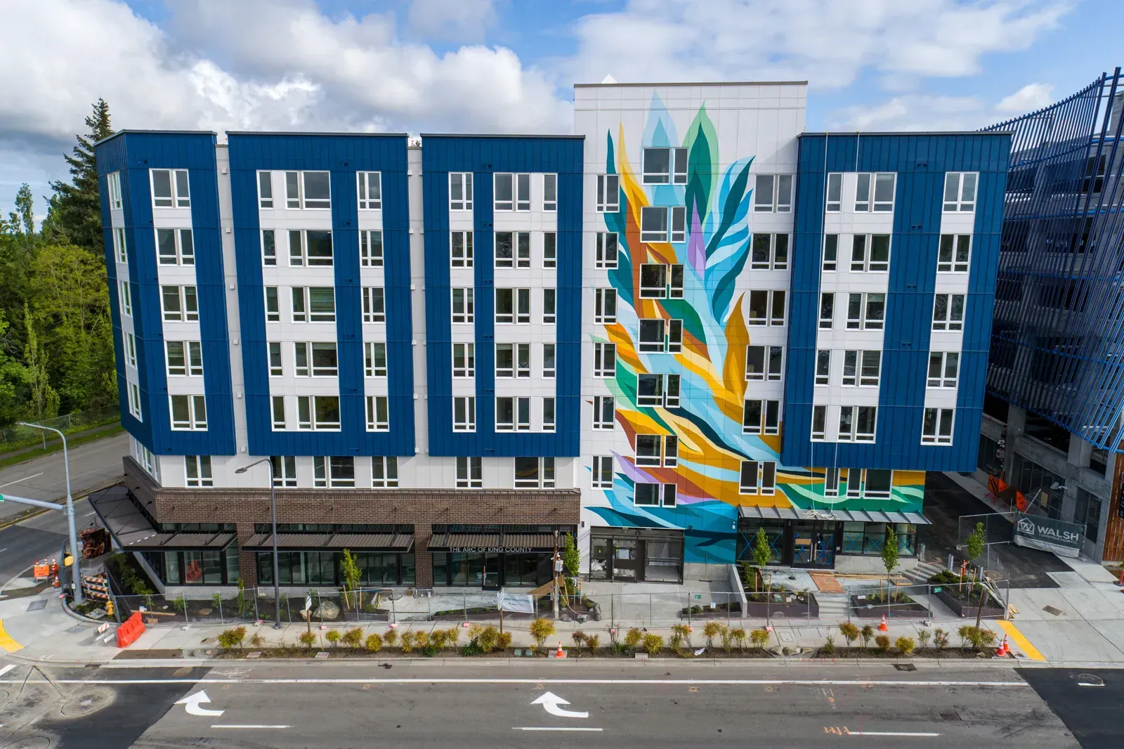 Multi-story blue and white apartment building with a colorful mural on the facade, street-level retail space.