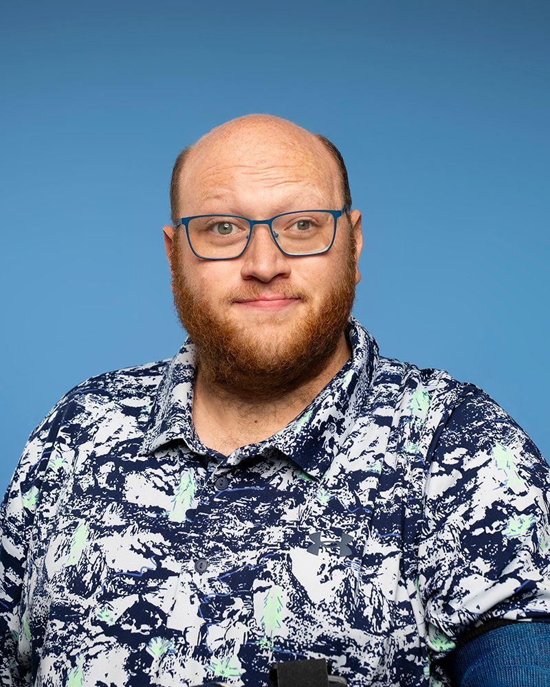 Bald man wearing glasses with blue glasses in front of a blue background.