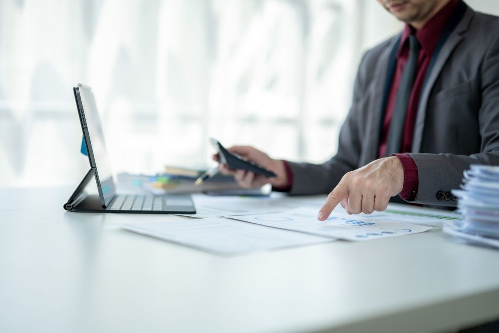 A man is sitting at a desk using a tablet, a cell phone and calculator.
