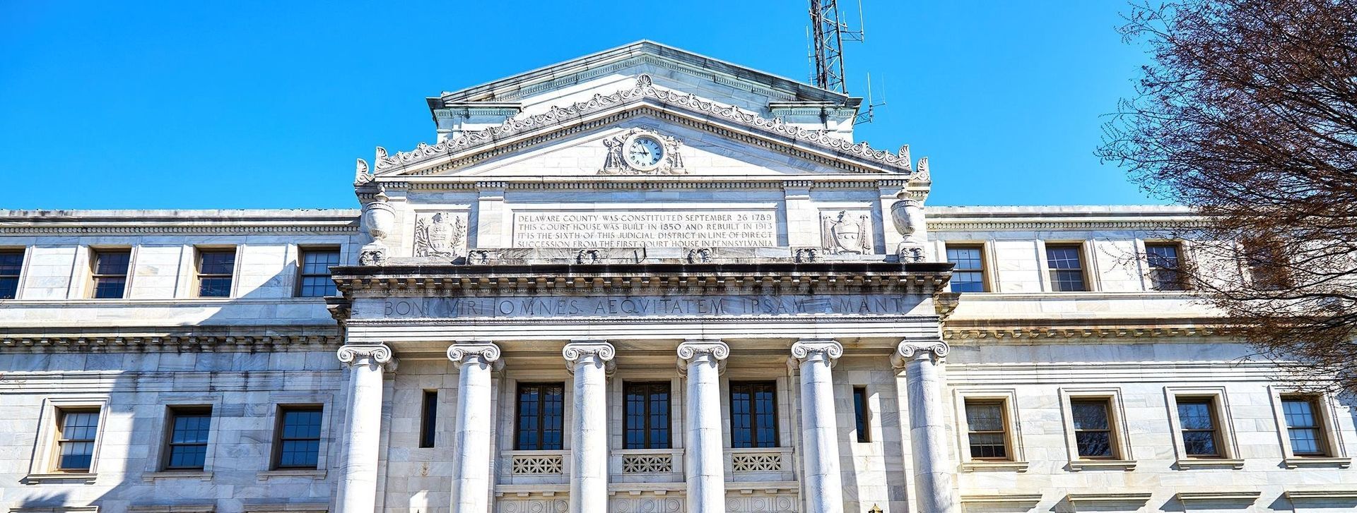 Stone government building with columns and a triangular pediment under a bright blue sky