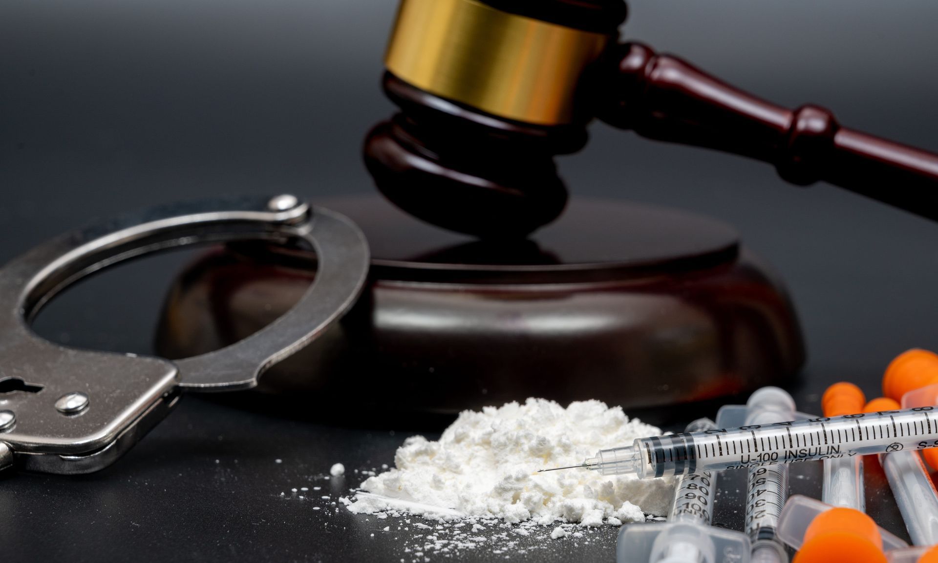 Gavel, handcuffs, and drug powder with capsules on a dark surface, symbolizing crime and drug trafficking