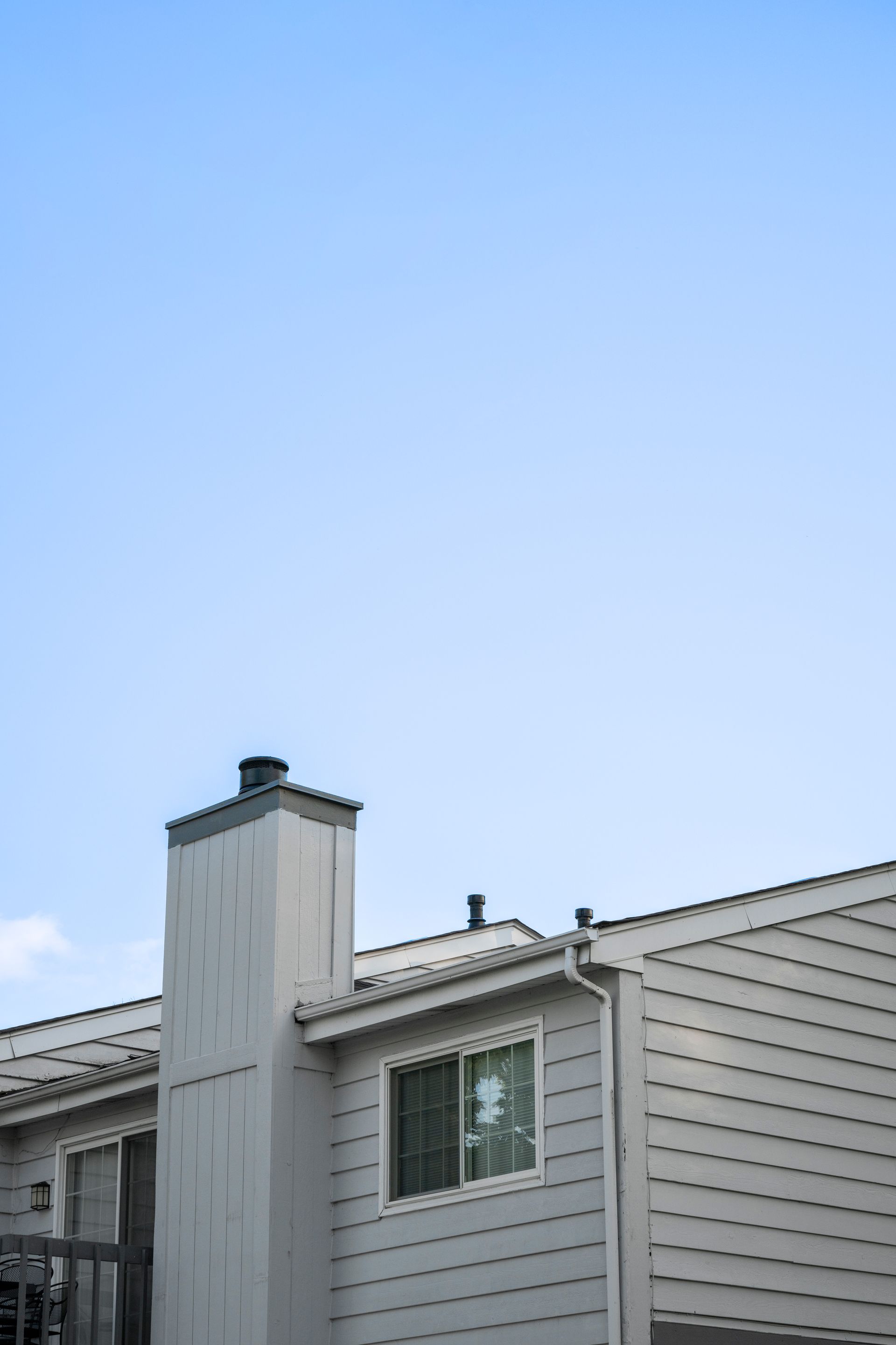 Gray two-story house with a chimney against a blue sky.
