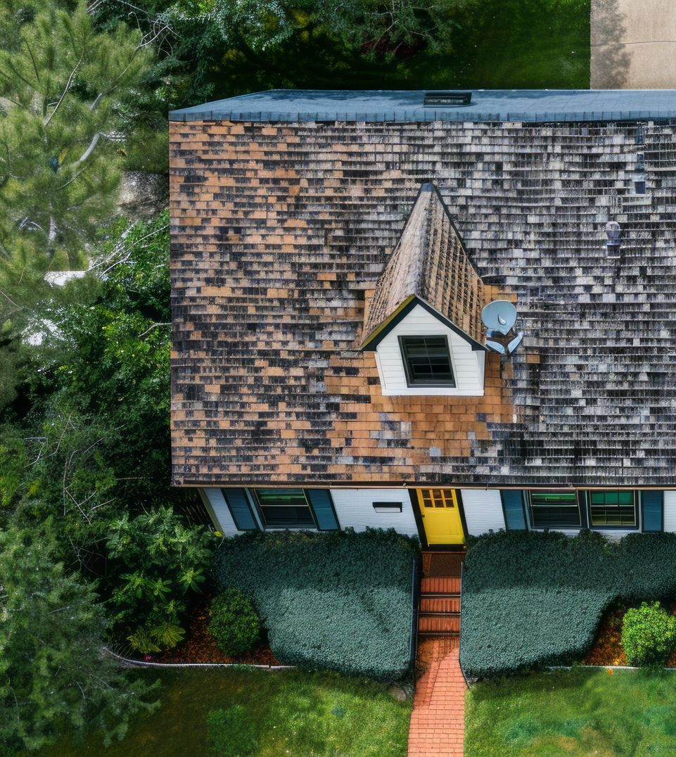 Aerial view of a house with a brown shingled roof, a dormer, and a yellow front door. 