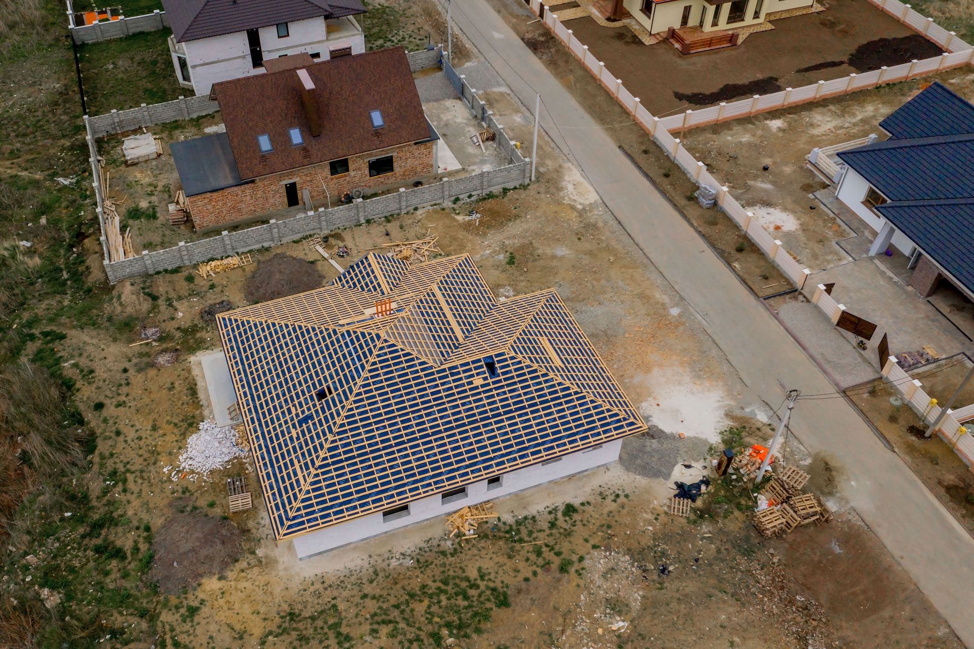 Aerial view of a house under construction with roof beams and surrounding neighborhood.