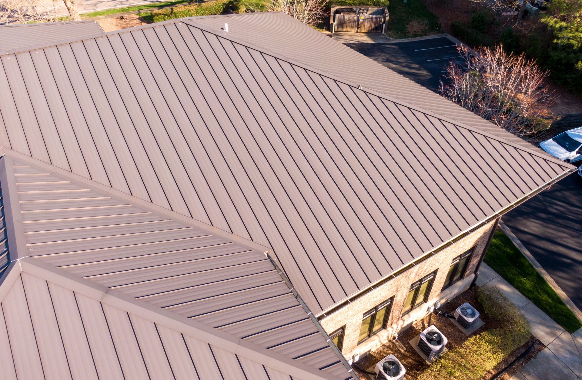 Brown metal roof of a building with visible ridges. Overlooks a parking lot and a few pieces of equipment.