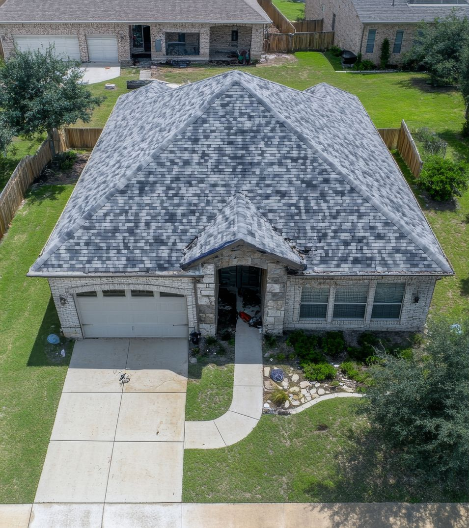 Aerial view of a single-story house with gray shingle roof, stone exterior, and attached garage.