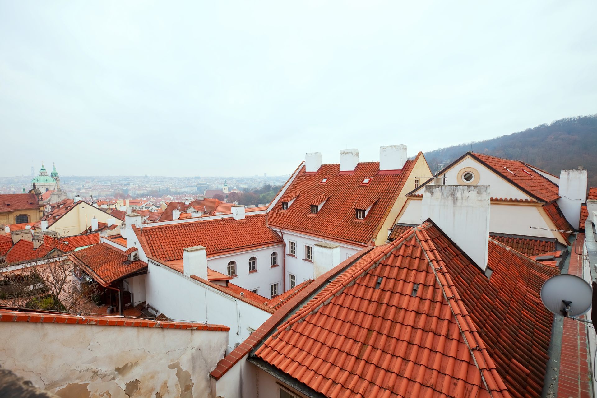 Overhead view of red-tiled roofs and white buildings against a cloudy sky in a European city.