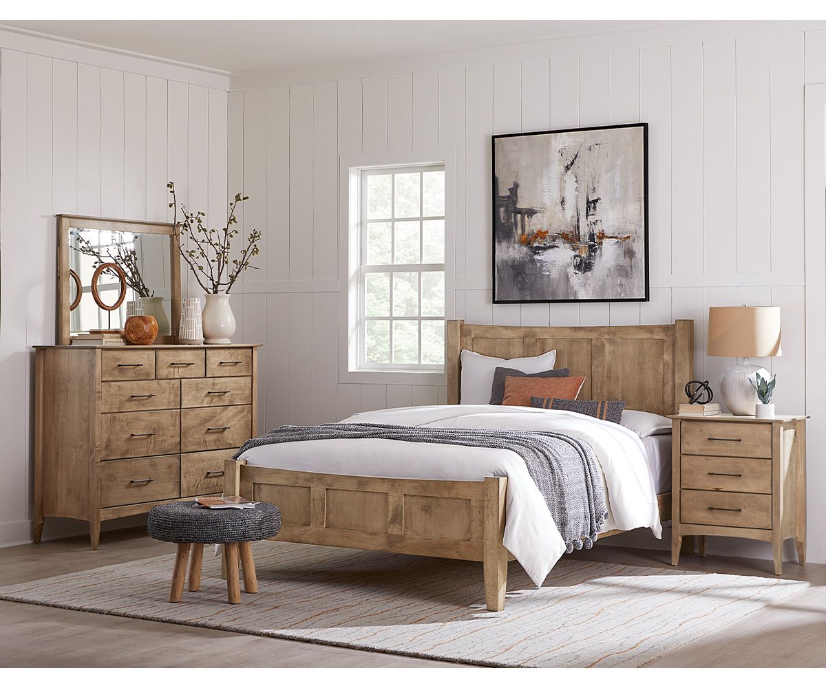 Bedroom with wooden furniture: bed, dresser with mirror, nightstand, and small stool on a rug.