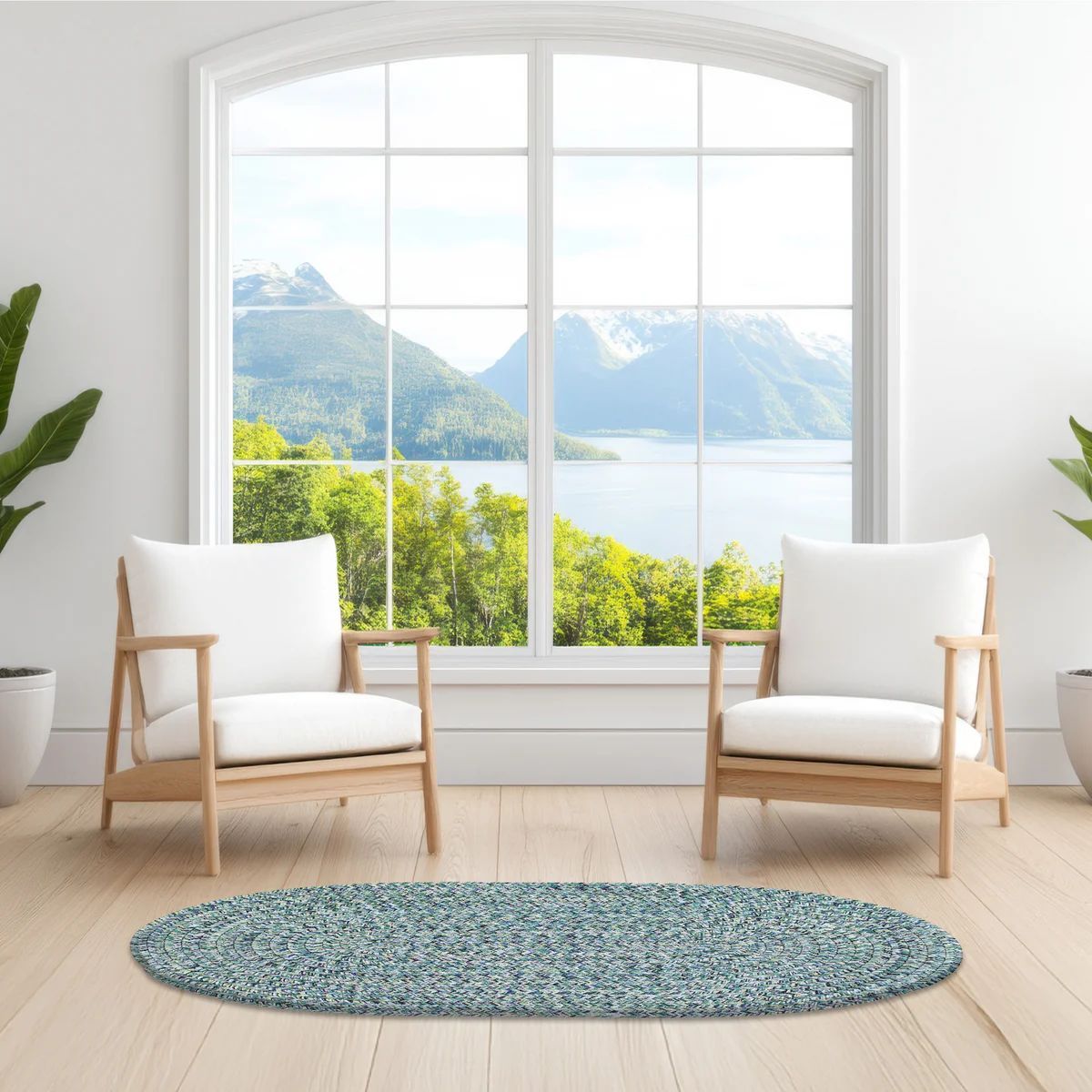 Two white armchairs face a large window overlooking a lake and mountains; blue oval rug on wood floor.