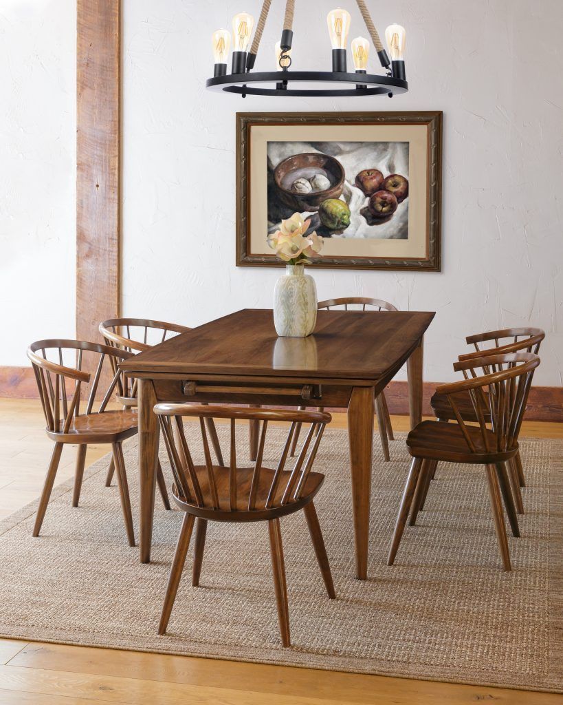 Dining room with wooden table, chairs, artwork, and chandelier on a jute rug.
