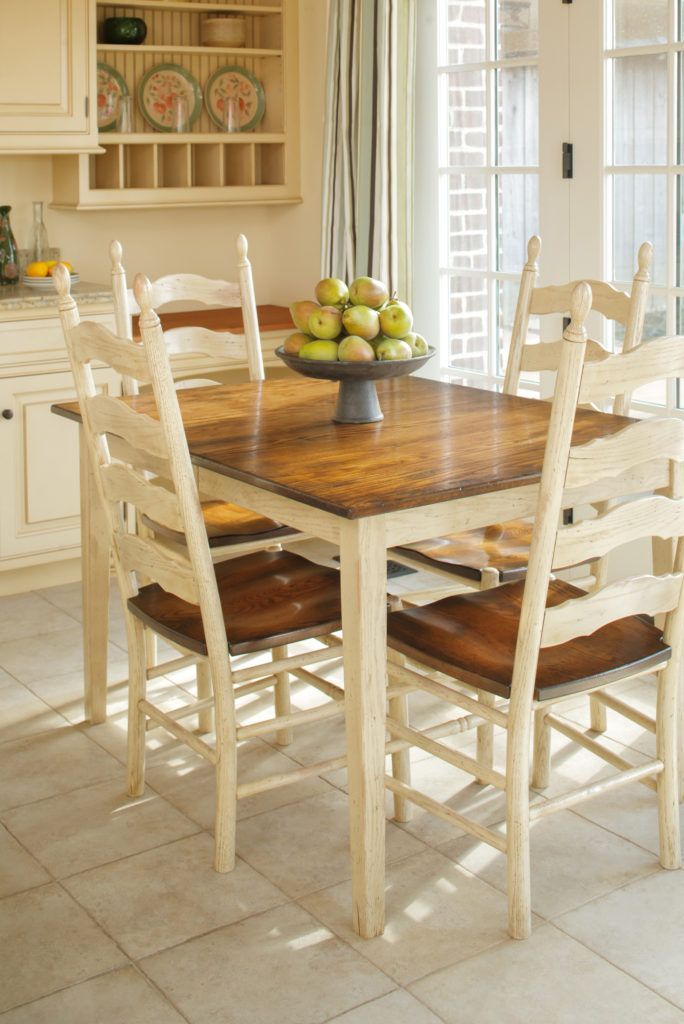 Dining table with four chairs in a bright kitchen; a bowl of fruit sits in the center.