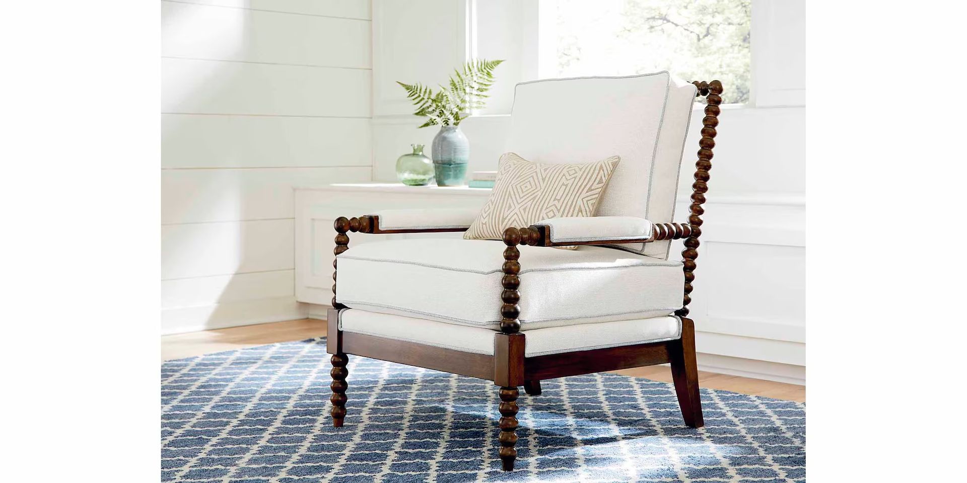 White armchair with dark wood frame, sitting on a blue patterned rug, next to a white wall.