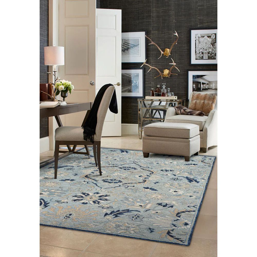 Room with a patterned blue rug, desk, chair, seating area with chair, and art on the wall.