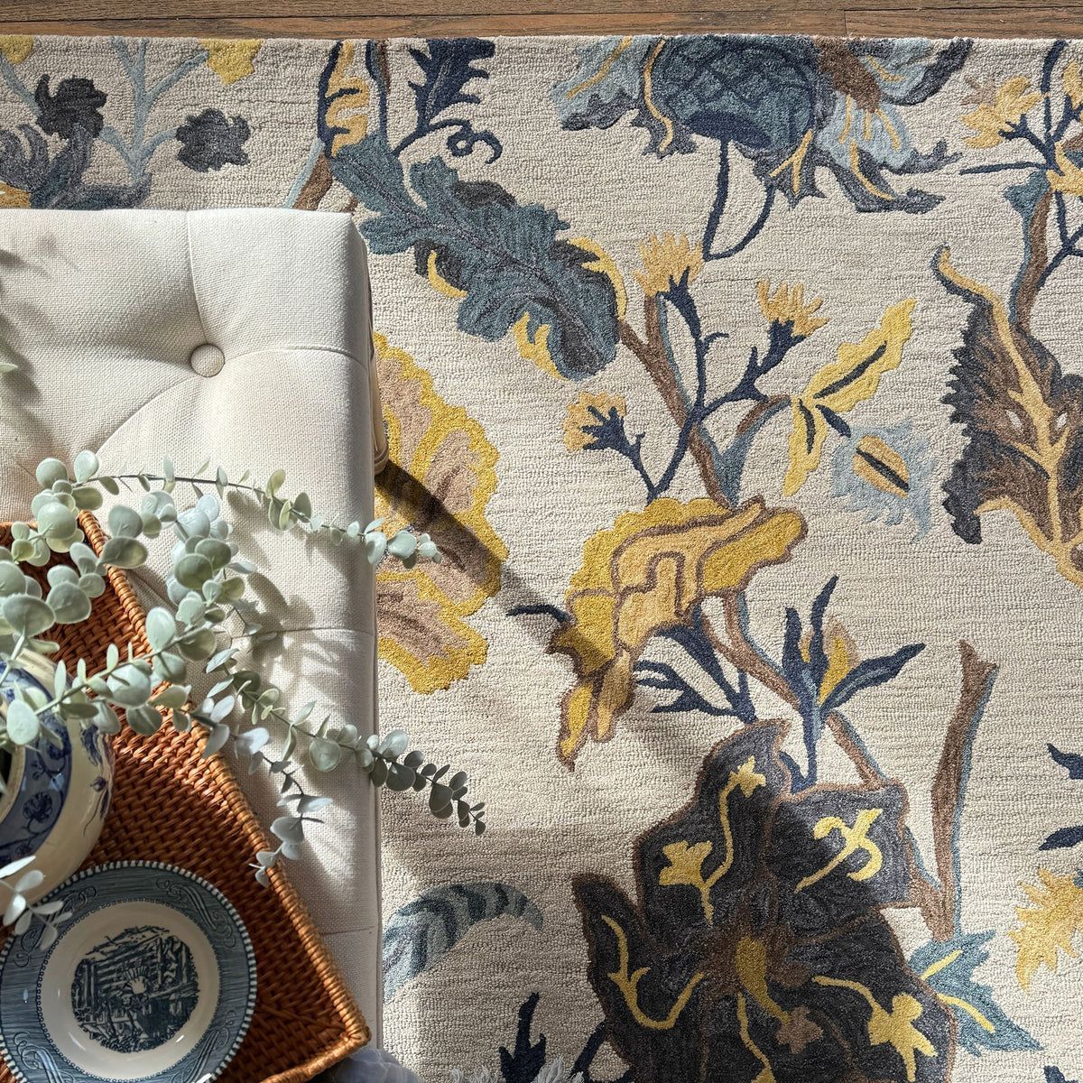 Overhead view of a floral rug with gold, blue, and brown accents; bench, plants, and dishes.