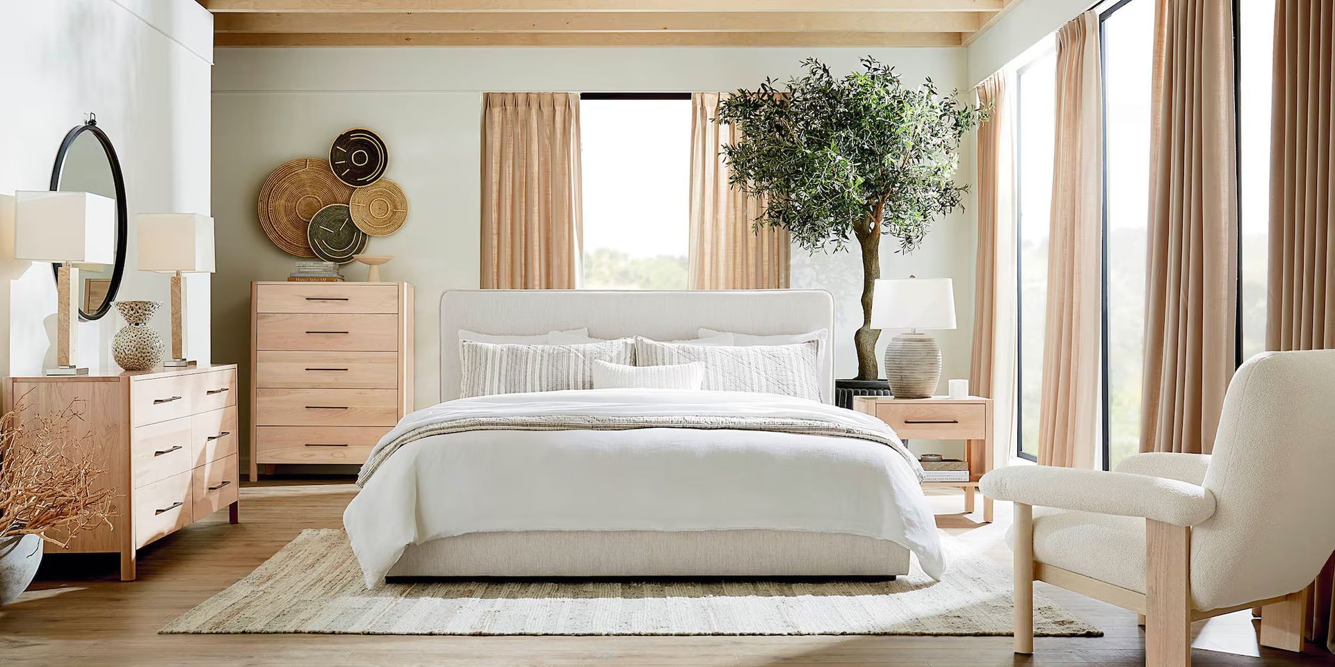 Bedroom with neutral tones, bed, chest of drawers, chair, large window with curtains, and large olive tree.